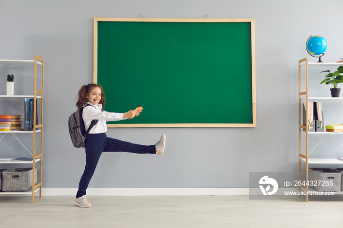 Back to school. Funny schoolgirl with a book is walking on the background of the school blackboard.