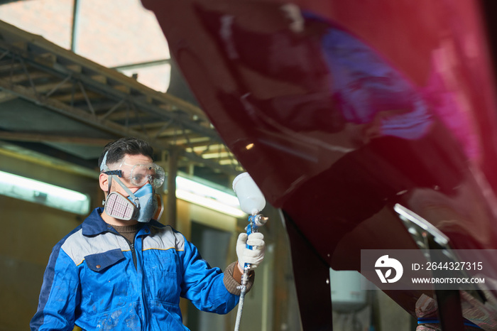 Portrait of man wearing protective mask painting boat using paint sprayer in yacht workshop at factory, copy space