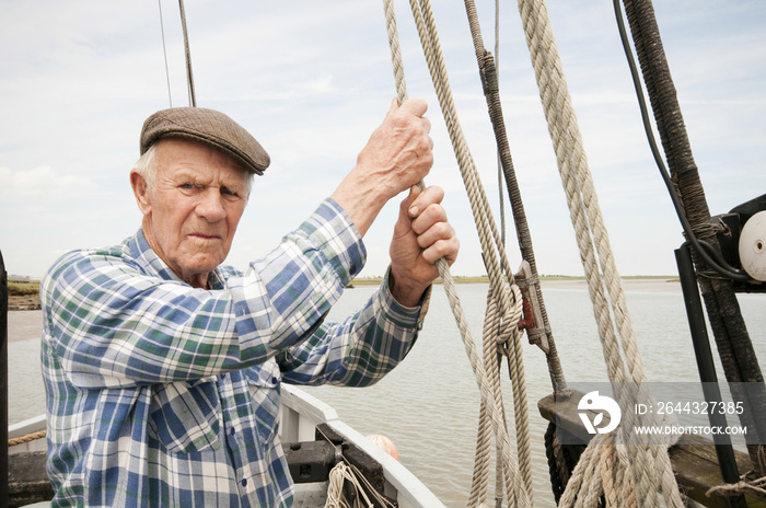 Portrait of a senior fisherman pulling rope on deck of a boat