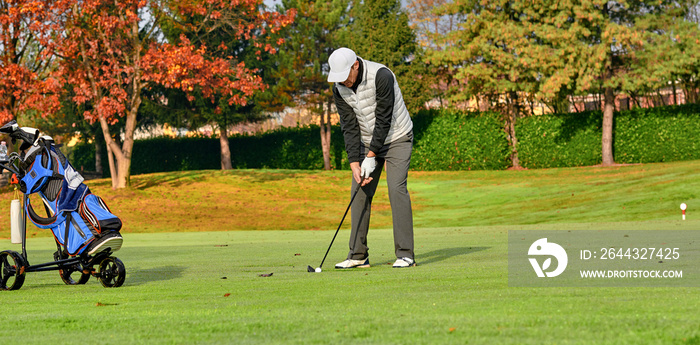 Golfer on a golf course in winter with wet grass, hitting the ball with a golf club.