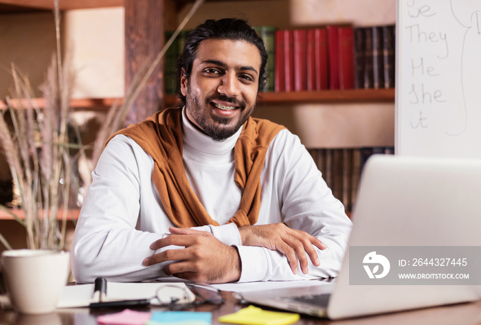 Successful Indian Teacher Sitting At Laptop Posing In Library Indoors