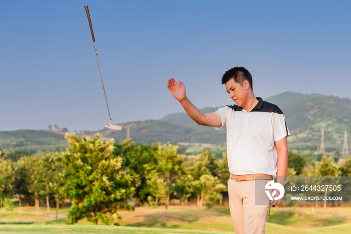 Asian golfer young man standing and angry gesture by thrown away putter on green in golf course after putting golf ball not hole.