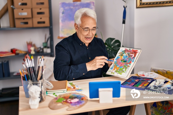 Senior man having online draw lesson sitting on table at art studio