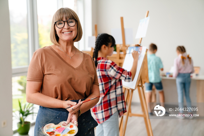 White teacher wearing eyeglasses smiling during class in art school