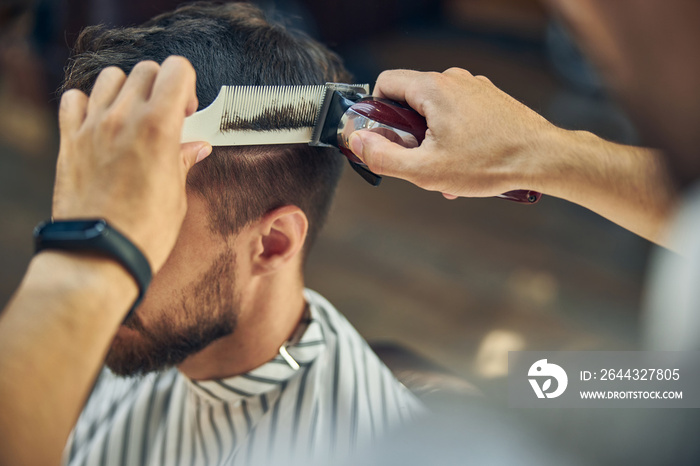 Skillful hair-stylist using electric hair clipper to cut hair