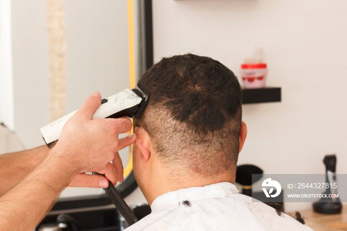 Back view of man getting short hair trimming at barber shop with clipper machine