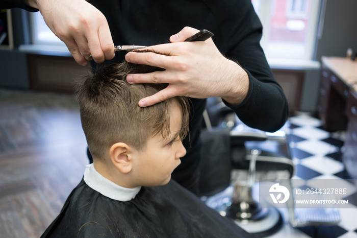 Little boy on a haircut in the barber sits on a chair.