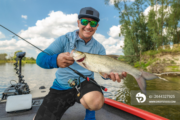 Success fishing. Fisherman with asp aspius fish on boat at wild river