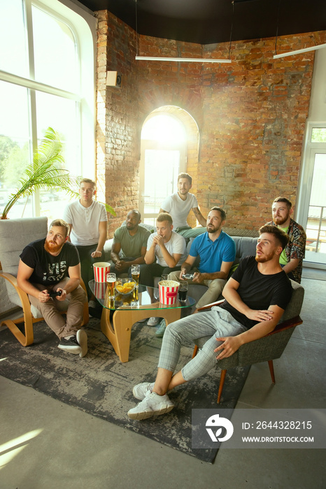 Group of excited friends playing video games at home. Caucasian male gamers or fans spending time and having fun together at home. Emotional watching gameplay. Modern technologies, friendship, weekend