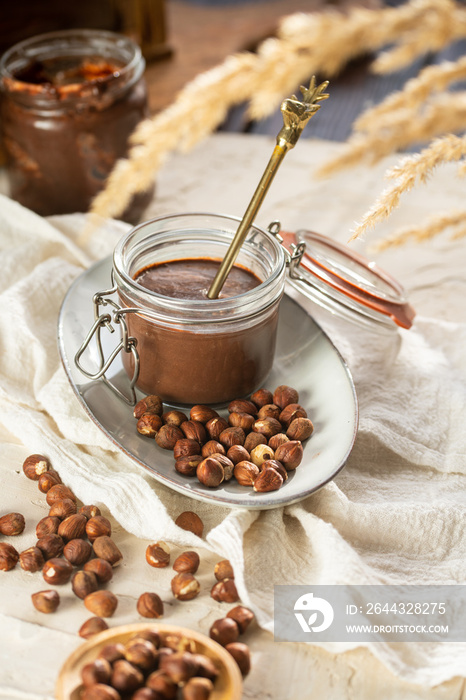 Homemade hazelnut cocoa chocolate cream in mason jar on plate surrounded by hazelnuts