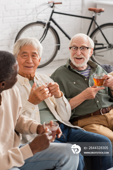 Positive interracial men holding cups of tea at home.