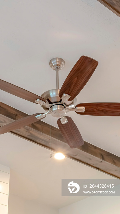 Vertical Ceiling fan with lights between decorative wood beams inside living room of home