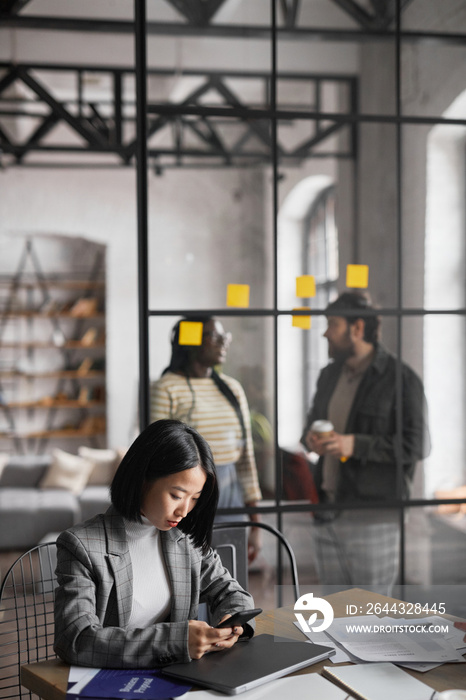 Vertical portrait of elegant Asian businesswoman working at table in graphic grey office interior, copy space