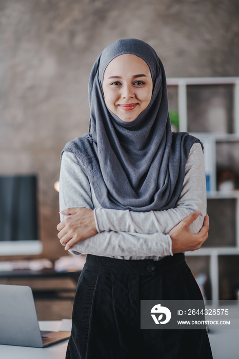 Portrait of a Muslim business woman happily looking at the camera in a hijab at work. smiling arab woman taking notes and work on laptop