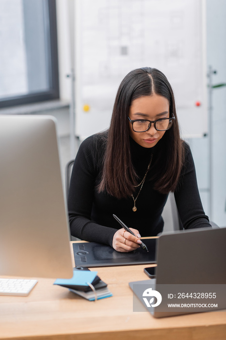 Asian interior designer using graphic tablet near laptop and computer in office.