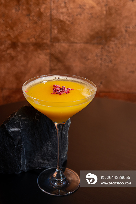 Glass of orange cocktail decorated with lemon at bar counter background.