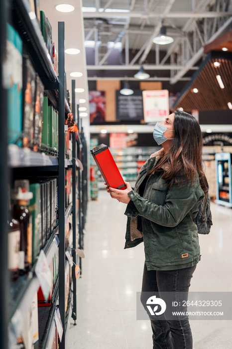 mature latin woman with mask choosing or buying drink in a supermarket