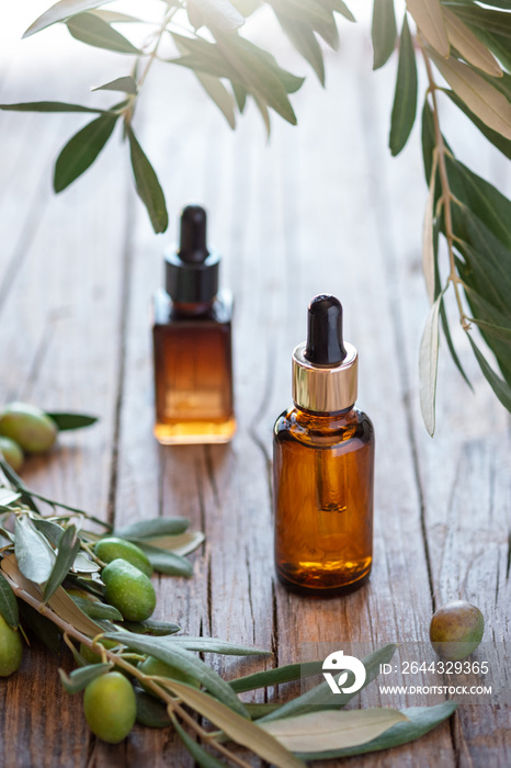 Olive based cosmetic amber bottles with serum or lotion on wooden background with sprig branches from olive tree.