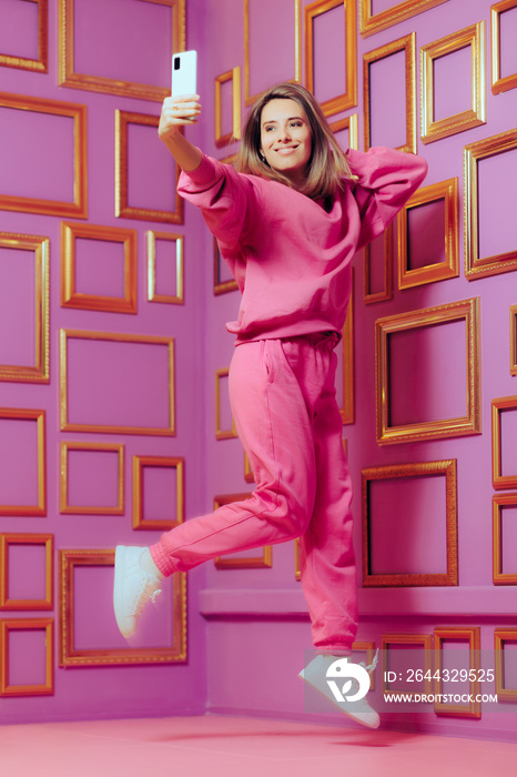 Jumping Woman Taking a Selfie in Front of Empty Photo Frames. Cheerful girl wearing athleisure tracksuit feeling confident and excited