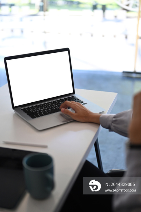 Cropped shot of young female sitting in modern office and using laptop searching information.