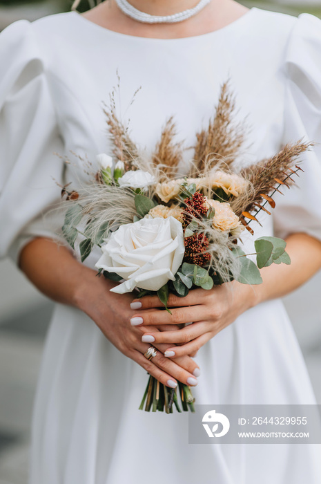 Portrait of a beautiful bride in a white long dress with an autumn bouquet of flowers, wild flowers, with a golden ring on her finger. Close-up wedding photography.