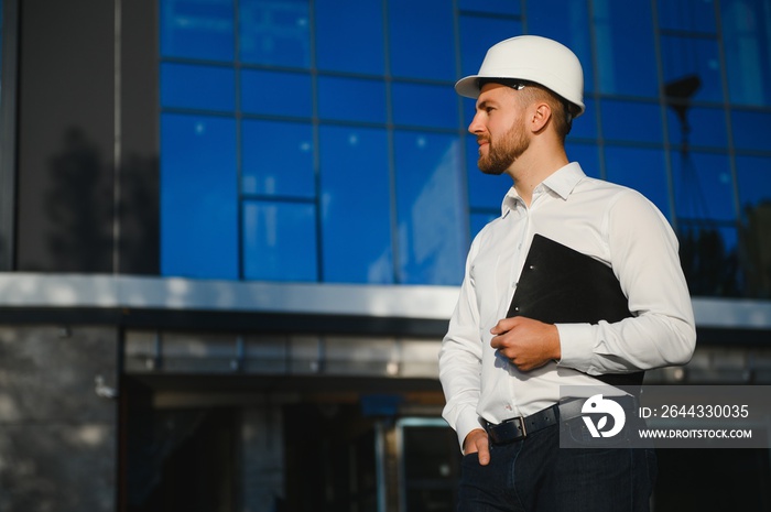 Successful engineer or architect, crane and building construction at backgrpound. Joyous businessman with wearing helmet.