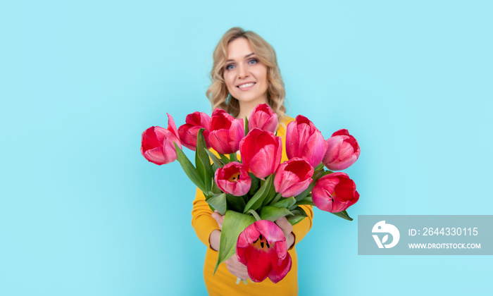 positive young woman with spring tulip flowers on blue background. march 8