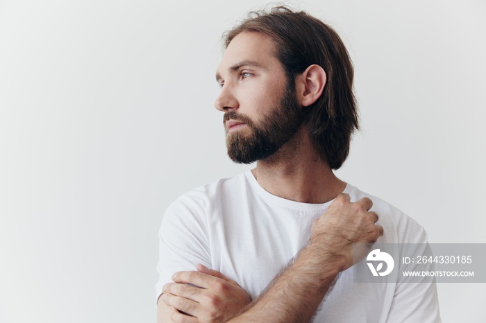 Portrait of a man with a black thick beard and long hair in a white T-shirt on a white isolated background emotion of sadness and longing