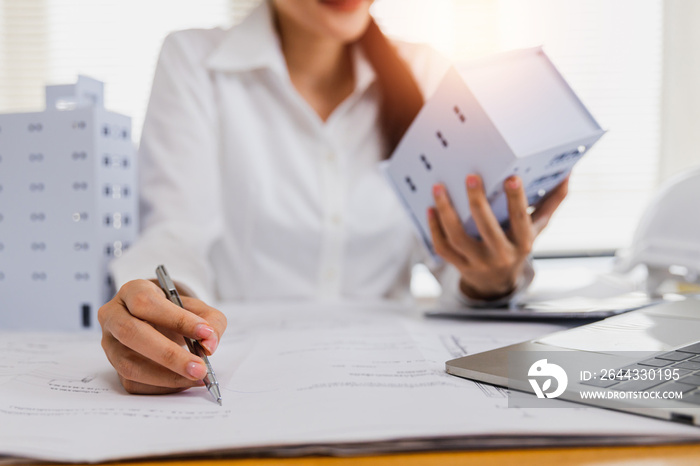 close up hand of engineer architect woman check correction on blue print and holding building model