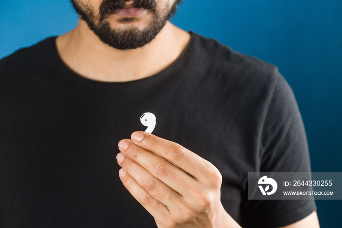 bearded man holding an airpod isolated on a blue background