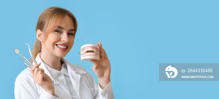 Female dentist with plastic jaw model and tools on blue background with space for text