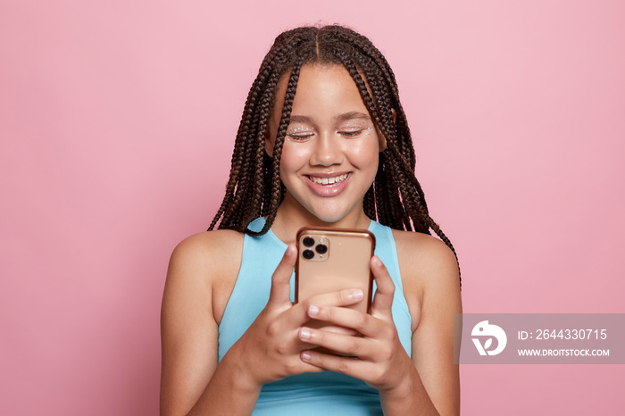 Studio shot of smiling girl with braids looking at smart phone