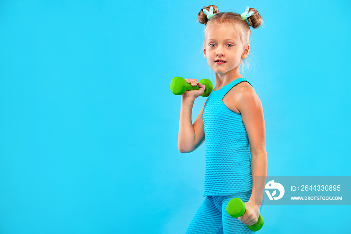 Kid girl doing fitness or yoga exercises with dumbbells isolated on blue background