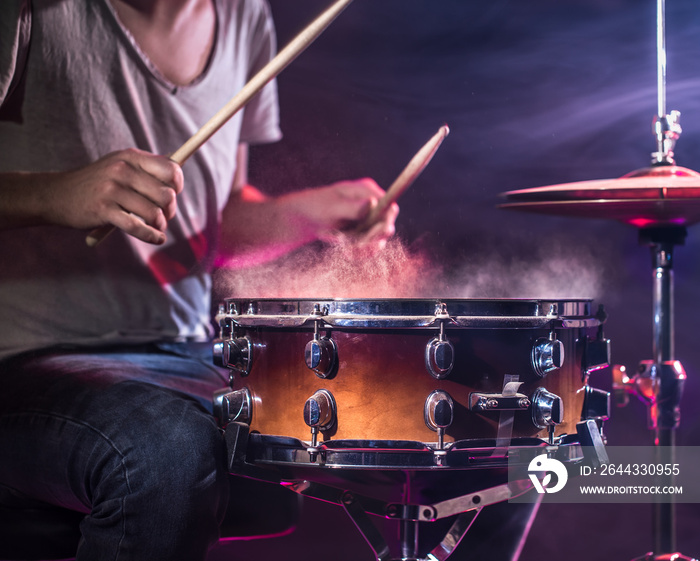 The drummer plays the drums. Beautiful blue and red background, with rays of light. Beautiful special effects smoke and lighting. The process of playing a musical instrument. Close-up photo.