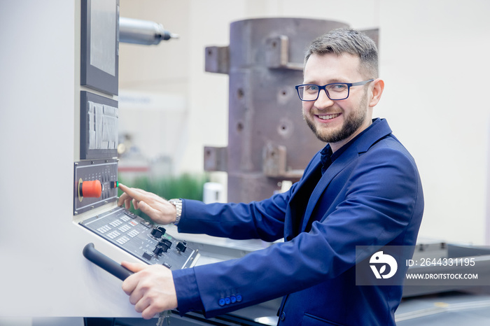 Engineer young man in glasses operates CNC automatic metalworking lathe or laser, industrial worker in modern factory