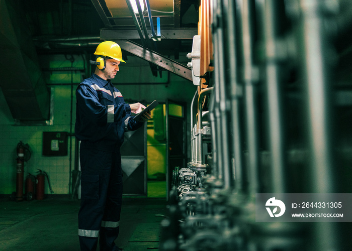 Portrait of young Caucasian man dressed in work wear using tablet while standing in heating plant.