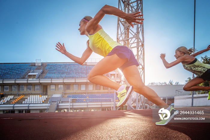 Two female sprinter athletes running on the treadmill race during training in athletics stadium.