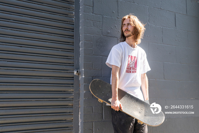 Young man standing outdoors holding skateboard