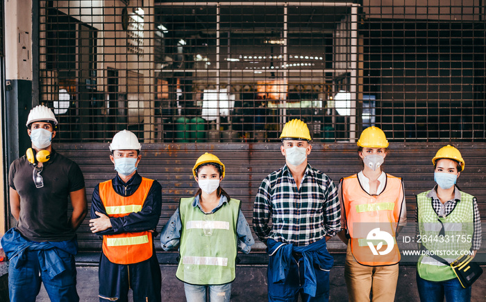 Group of industrial or engineer corporate workers wear protective mask and hard hat helmet standing line up in front of factory lock down prevention for Coronavirus or COVID-19 epidemic outbreak