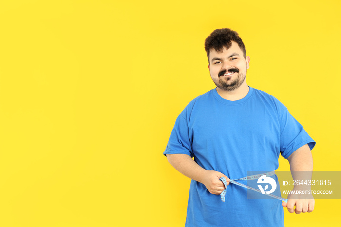 Concept of weight loss, fat guy with measuring tape on yellow background