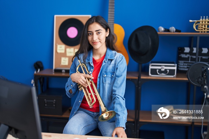 Young hispanic girl musician holding trumpet at music studio