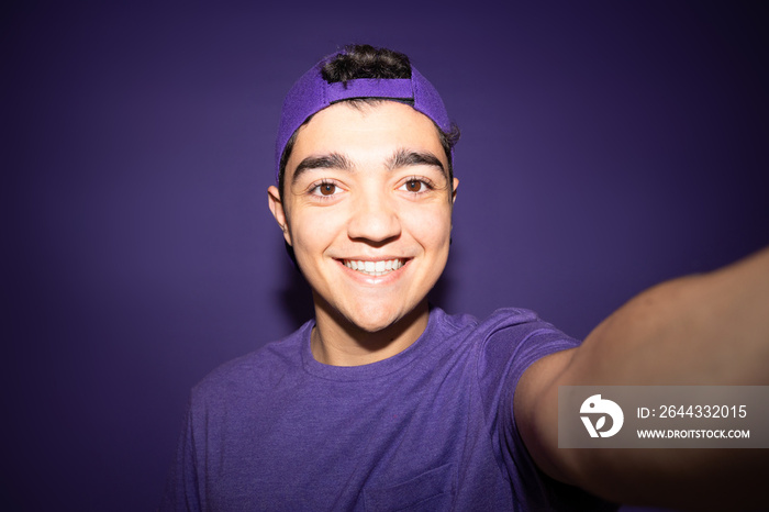 Hispanic teenager boy taking selfie isolated on purple background