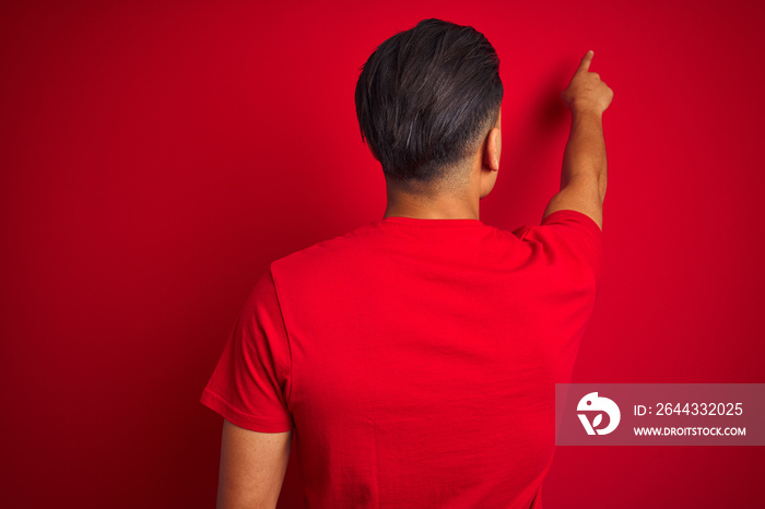 Young brazilian man wearing t-shirt standing over isolated red background Posing backwards pointing ahead with finger hand