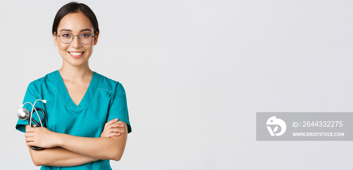 Covid-19, coronavirus disease, healthcare workers concept. Close-up of confident professional female doctor, nurse in glasses and scrubs standing white background, cross arms