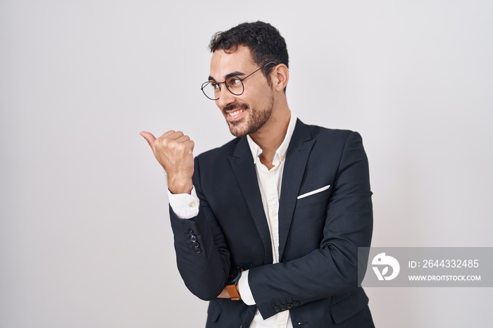 Handsome business hispanic man standing over white background smiling with happy face looking and pointing to the side with thumb up.