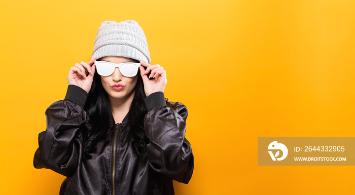 Fashionable woman with attitude in bomber jacket and sunglasses on a yellow background