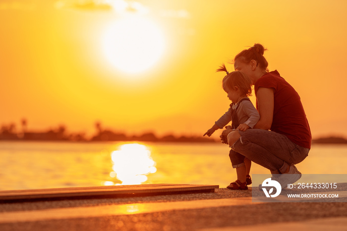 Mom and daughter are sitting on the embankment at sunset. The family is resting on the embankment on a summer evening. Family outing