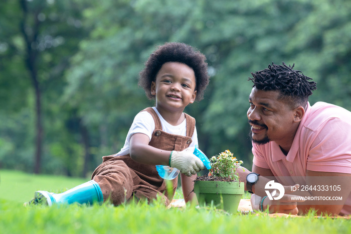 Dark-skinned boy and his father spent time outdoors on summer days, boy learning to plant trees and looking at camera