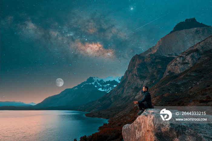 silhouette of a man sitting meditating on a rock over the lake with mountains and Milky Way  background in Torres del Paine National Park