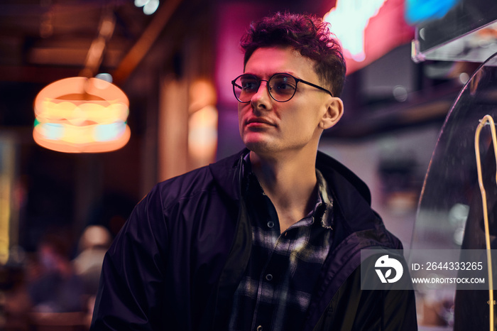 A handsome young man standing at night in the street. Illuminated signboards, neon, lights.